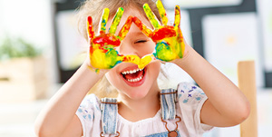 Fachkraft in Kindertagesstätten: Kind mit bunten Händen lacht vergnügt